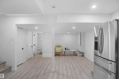 This open space features light-toned flooring, recessed lighting, and a stainless steel refrigerator - Edmonton, AB - Indoor Photo Showing Other Room