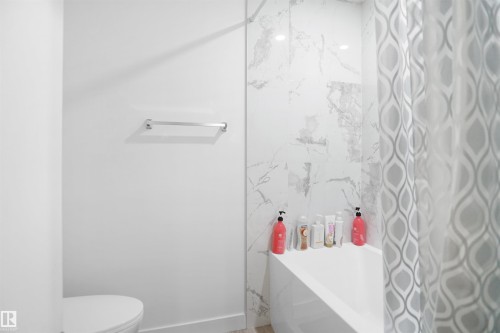 Bathroom featuring a white bathtub, a shower curtain with a geometric pattern, a towel bar, and white wall tiles with a grey marble-like pattern - Edmonton, AB - Indoor Photo Showing Bathroom