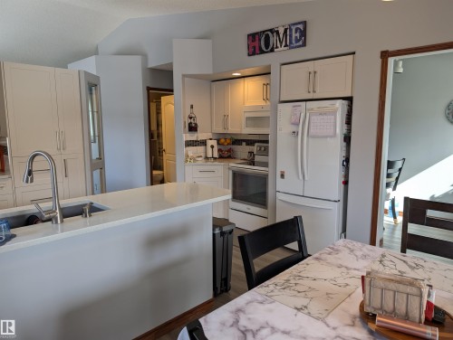 The kitchen features white cabinetry, a kitchen island with an undermount sink, and stainless steel appliances including a refrigerator and range - 65 Coloniale Way, Beaumont, AB - Indoor Photo Showing Kitchen With Double Sink