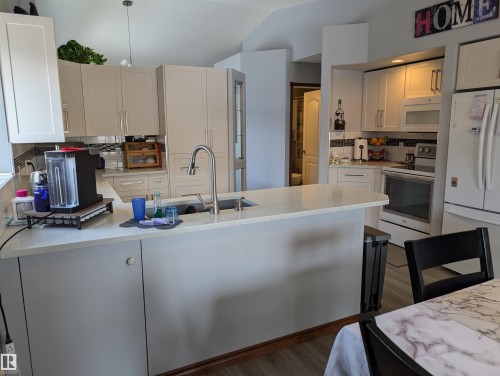 The kitchen features light-colored cabinetry, a large kitchen island with a sink, and stainless steel appliances including a refrigerator and range - 65 Coloniale Way, Beaumont, AB - Indoor Photo Showing Kitchen With Double Sink