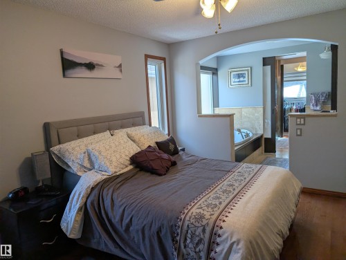 The bedroom features a ceiling fan, a window with wood trim, and a bed with a tufted headboard - 65 Coloniale Way, Beaumont, AB - Indoor Photo Showing Bedroom