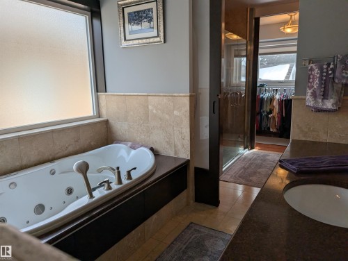 Bathroom featuring a jetted tub with polished chrome fixtures, a frosted window, and stone-tiled walls - 65 Coloniale Way, Beaumont, AB - Indoor Photo Showing Bathroom