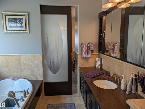 The bathroom features a built-in tub, a vanity with an integrated sink, and an expansive mirror - 65 Coloniale Way, Beaumont, AB - Indoor Photo Showing Bathroom