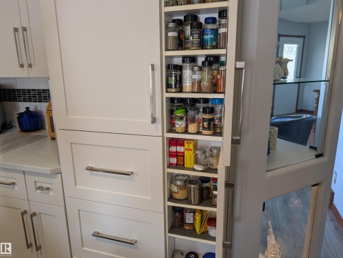 The kitchen features white cabinetry with brushed nickel hardware, a dark tiled backsplash, and a light-colored countertop - 65 Coloniale Way, Beaumont, AB - Indoor