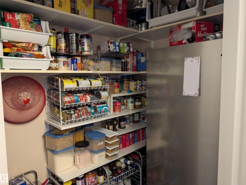Pantry featuring extensive shelving for storage, a stainless steel refrigerator, and a wall-mounted can organizer - 65 Coloniale Way, Beaumont, AB - Indoor
