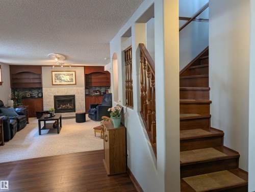 This property features a living room with an integrated fireplace and built-in shelving, complemented by a staircase with wooden treads and balusters - 65 Coloniale Way, Beaumont, AB - Indoor Photo Showing Other Room With Fireplace