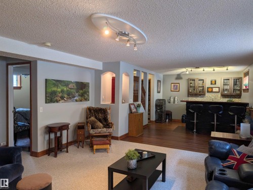 This spacious room features light-colored carpeting, hardwood flooring, and a dedicated bar area with a backsplash and three bar stools - 65 Coloniale Way, Beaumont, AB - Indoor Photo Showing Living Room