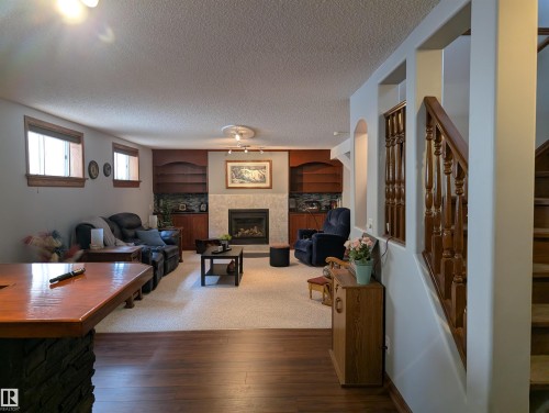 The property features a spacious living area with hardwood flooring, a gas fireplace with stone surround, and built-in shelving units - 65 Coloniale Way, Beaumont, AB - Indoor Photo Showing Living Room With Fireplace