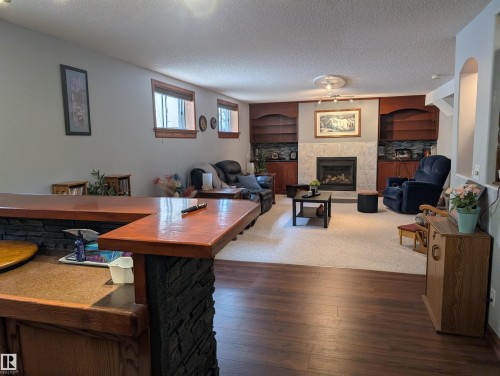 The property features a spacious room with hardwood flooring, a stone-faced bar area, a carpeted living space with a fireplace, built-in shelving, and windows with wood trim - 65 Coloniale Way, Beaumont, AB - Indoor Photo Showing Living Room With Fireplace