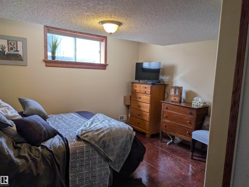 This room features light-colored walls, a window with wood trim, and a ceiling light fixture - 65 Coloniale Way, Beaumont, AB - Indoor Photo Showing Bedroom
