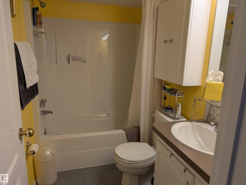 Bathroom featuring a white bathtub with an overhead shower and a white vanity with a single sink and an overhead cabinet - 65 Coloniale Way, Beaumont, AB - Indoor Photo Showing Bathroom