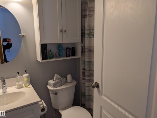 Bathroom featuring a white vanity with a rectangular sink, a round mirror, and a toilet - 65 Coloniale Way, Beaumont, AB - Indoor Photo Showing Bathroom