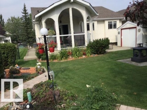 The property features a well-maintained lawn, a screened-in porch with arched openings, and a storage shed with red trim - 65 Coloniale Way, Beaumont, AB - Outdoor