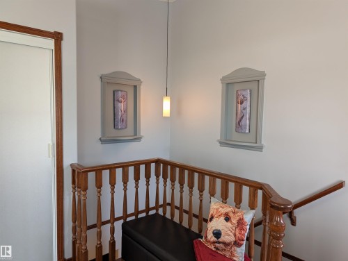The property features an interior staircase with a wooden banister and white balusters, a pendant light fixture, and two decorative wall hangings - 65 Coloniale Way, Beaumont, AB - Indoor Photo Showing Other Room
