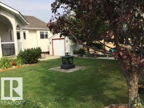 The property features a well-maintained lawn, a paved patio area, and a storage shed with a white door and red trim - 65 Coloniale Way, Beaumont, AB - Outdoor