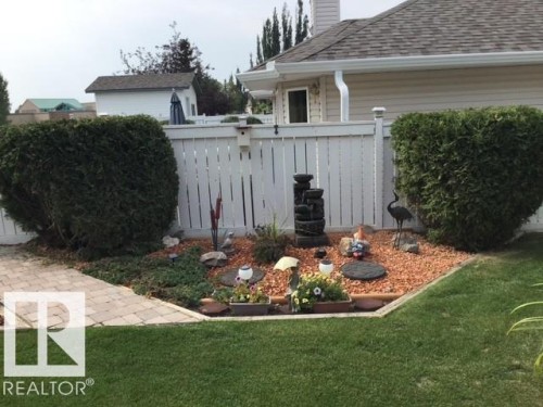 The property features a well-maintained lawn, a decorative garden bed with various plants and a water feature, and a paved walkway - 65 Coloniale Way, Beaumont, AB - Outdoor