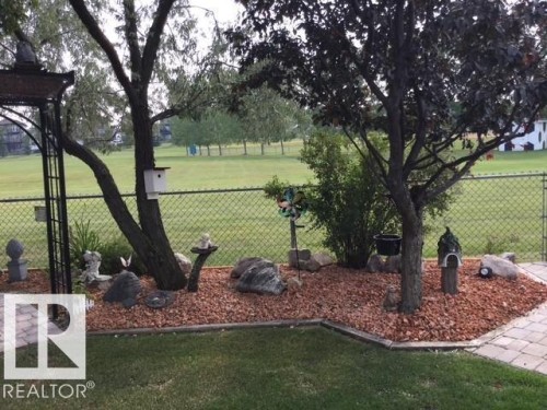 The property features a landscaped yard with a lawn, mature trees, and decorative rock beds - 65 Coloniale Way, Beaumont, AB - Outdoor