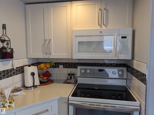The kitchen features white shaker-style cabinetry, a white microwave, and a white electric range with a black cooktop - 65 Coloniale Way, Beaumont, AB - Indoor Photo Showing Kitchen