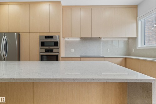 The kitchen features light wood cabinetry, stainless steel appliances including a refrigerator and built-in ovens, and light-colored countertops - 14037 104 Avenue, Edmonton, AB - Indoor Photo Showing Kitchen