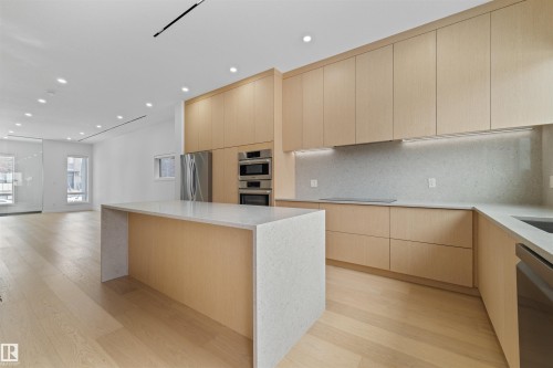 Modern kitchen featuring light wood cabinetry, a large island with a light-colored countertop, and stainless steel appliances including a refrigerator and double wall ovens - 14037 104 Avenue, Edmonton, AB - Indoor Photo Showing Kitchen