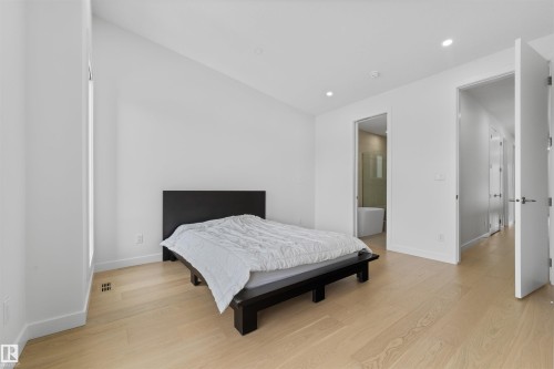 Well-lit room featuring light-colored hardwood flooring, white walls, recessed lighting, and a modern style door with a dark handle - 14037 104 Avenue, Edmonton, AB - Indoor Photo Showing Bedroom
