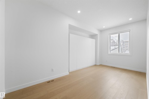 A brightly lit interior space featuring light-toned hardwood floors, white walls, recessed ceiling lighting, and a window with blinds - 14037 104 Avenue, Edmonton, AB - Indoor Photo Showing Other Room