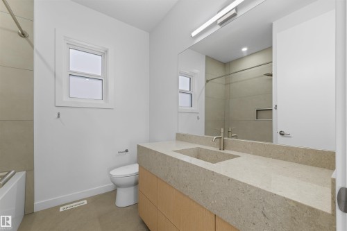 Bathroom featuring a light-colored countertop with an integrated rectangular sink, a large mirror, and a modern vanity with light wood cabinetry - 14037 104 Avenue, Edmonton, AB - Indoor Photo Showing Bathroom