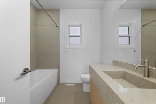 Bathroom featuring a built-in bathtub with tiled surround, a window, a vanity with an integrated sink, and a large mirror - 14037 104 Avenue, Edmonton, AB - Indoor Photo Showing Bathroom