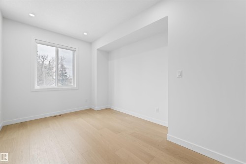 This room features light-toned hardwood flooring, recessed lighting, and a window with a view of trees - 14037 104 Avenue, Edmonton, AB - Indoor Photo Showing Other Room