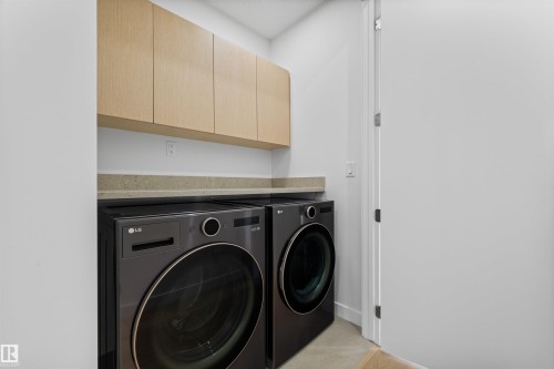 Utility area featuring light wood cabinetry, a light-colored countertop, and a front-loading washer and dryer - 14037 104 Avenue, Edmonton, AB - Indoor Photo Showing Laundry Room