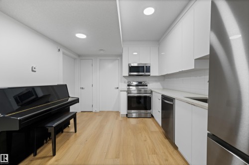 The property features light wood flooring, a kitchen area with white cabinetry, stainless steel appliances, and a light-colored countertop - 14037 104 Avenue, Edmonton, AB - Indoor Photo Showing Kitchen