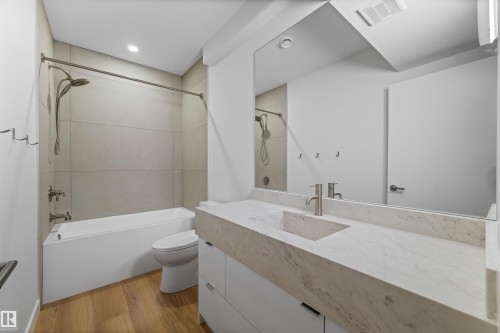 Contemporary bathroom featuring a bathtub with overhead shower, a vanity with an integrated sink and stone countertop, and wood floors - 14037 104 Avenue, Edmonton, AB - Indoor Photo Showing Bathroom