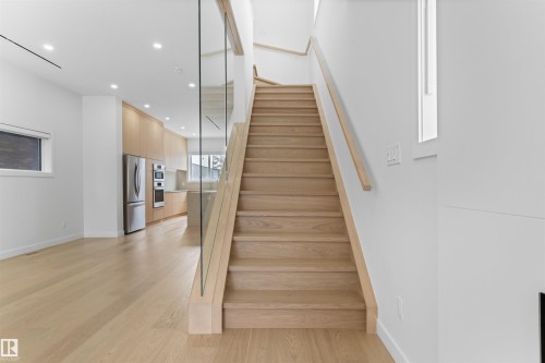 The property features a staircase with light wood treads and a glass railing, complementing the light wood floors - 14037 104 Avenue, Edmonton, AB - Indoor Photo Showing Other Room