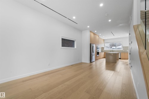 The open concept living area features light hardwood flooring, recessed lighting, and a modern kitchen with light wood cabinetry and stainless steel appliances - 14037 104 Avenue, Edmonton, AB - Indoor