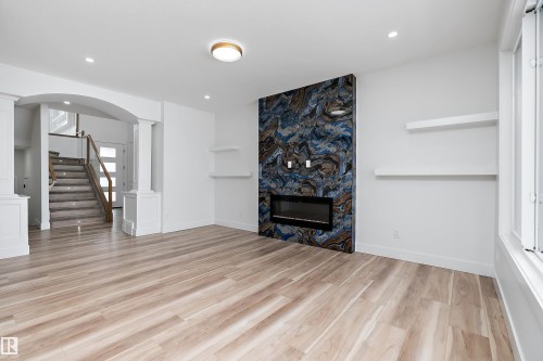 Expansive living area featuring light-toned flooring, a modern fireplace with a unique dark-toned accent wall, and recessed lighting - 219 Crystal Creek Dr, Leduc, AB - Indoor With Fireplace