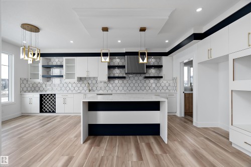 Modern kitchen featuring light wood flooring, white cabinetry, a kitchen island with a white countertop, and contemporary pendant lighting - 219 Crystal Creek Dr, Leduc, AB - Indoor Photo Showing Kitchen With Upgraded Kitchen