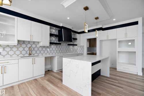The kitchen features white cabinetry with gold hardware, a white patterned backsplash, and a central island with a white countertop - 219 Crystal Creek Dr, Leduc, AB - Indoor Photo Showing Kitchen With Upgraded Kitchen