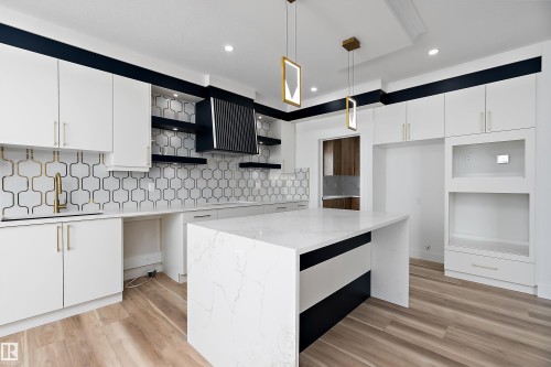 The kitchen features a large island with a white countertop, modern pendant lighting, and light wood flooring - 219 Crystal Creek Dr, Leduc, AB - Indoor Photo Showing Kitchen With Upgraded Kitchen