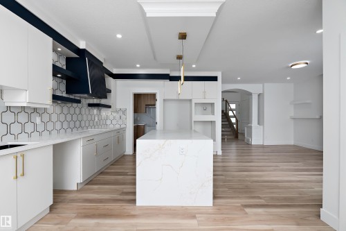 The kitchen features light wood flooring, white cabinetry with gold hardware, and a white countertop with a patterned backsplash - 219 Crystal Creek Dr, Leduc, AB - Indoor Photo Showing Kitchen With Upgraded Kitchen