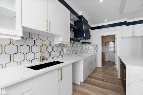 The kitchen features white cabinetry with gold-toned hardware, white countertops, and a black sink with a gold-toned faucet - 219 Crystal Creek Dr, Leduc, AB - Indoor Photo Showing Kitchen With Upgraded Kitchen