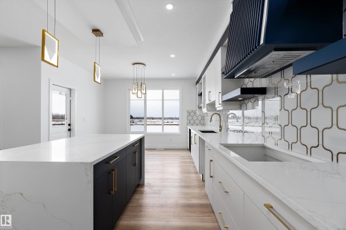 Contemporary kitchen featuring a large island with a white countertop and dark cabinetry, light wood flooring, and a decorative tile backsplash - 219 Crystal Creek Dr, Leduc, AB - Indoor Photo Showing Kitchen With Upgraded Kitchen
