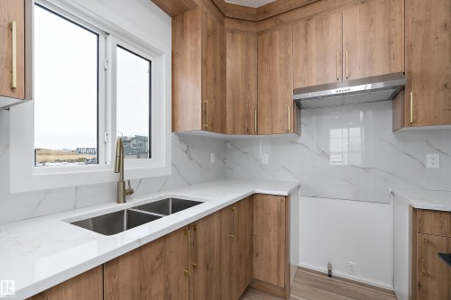 The kitchen features wood-look cabinetry with gold-toned hardware, white countertops, and a stainless steel double basin sink with a modern faucet - 219 Crystal Creek Dr, Leduc, AB - Indoor Photo Showing Kitchen With Double Sink