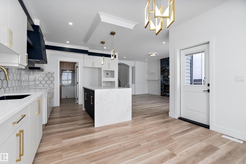 The kitchen features white cabinetry with gold-toned hardware, a white tile backsplash with a geometric pattern, and an island with a white countertop - 219 Crystal Creek Dr, Leduc, AB - Indoor Photo Showing Kitchen With Upgraded Kitchen