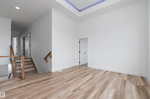 The property features light wood flooring, a tray ceiling with accent lighting, and a staircase with a glass and wood railing - 219 Crystal Creek Dr, Leduc, AB - Indoor Photo Showing Other Room