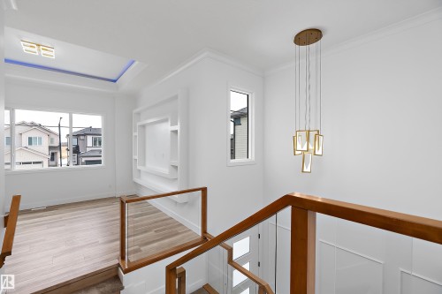 The property offers a contemporary interior with light wood flooring, a decorative ceiling feature with accent lighting, and a modern chandelier - 219 Crystal Creek Dr, Leduc, AB - Indoor Photo Showing Other Room
