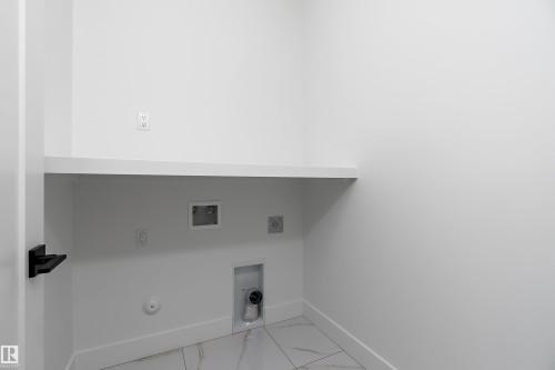 Utility area featuring a white floating shelf, tiled flooring, and a white door with a dark handle - 219 Crystal Creek Dr, Leduc, AB - Indoor