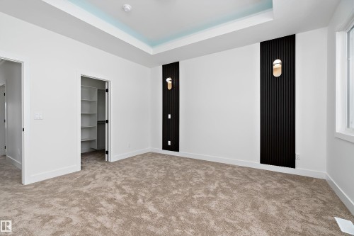 This room features soft carpet flooring, a tray ceiling with a light blue accent, and two decorative wall panels with sconce lighting - 219 Crystal Creek Dr, Leduc, AB - Indoor Photo Showing Other Room