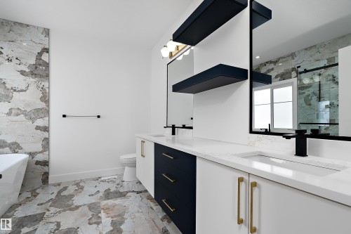 The bathroom features a dual vanity with white countertops, integrated sinks, and black and white cabinetry with gold handles - 219 Crystal Creek Dr, Leduc, AB - Indoor Photo Showing Bathroom