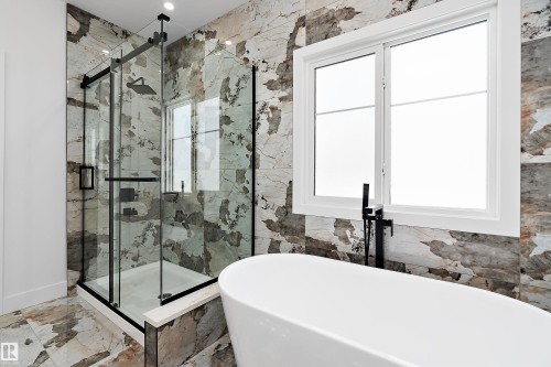 This bathroom features a spacious glass-enclosed shower with a rainfall showerhead, a freestanding soaking tub with a matte black floor-mounted faucet, and a large window - 219 Crystal Creek Dr, Leduc, AB - Indoor Photo Showing Bathroom