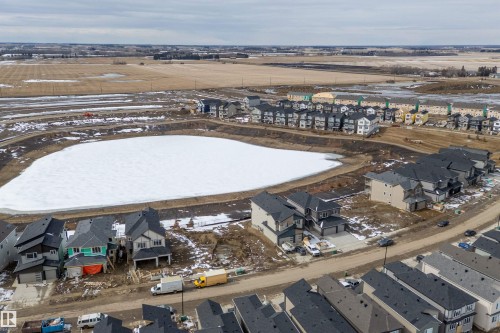 Aerial view of a residential area featuring a frozen pond, surrounding properties, and undeveloped land - 219 Crystal Creek Dr, Leduc, AB - Outdoor With View